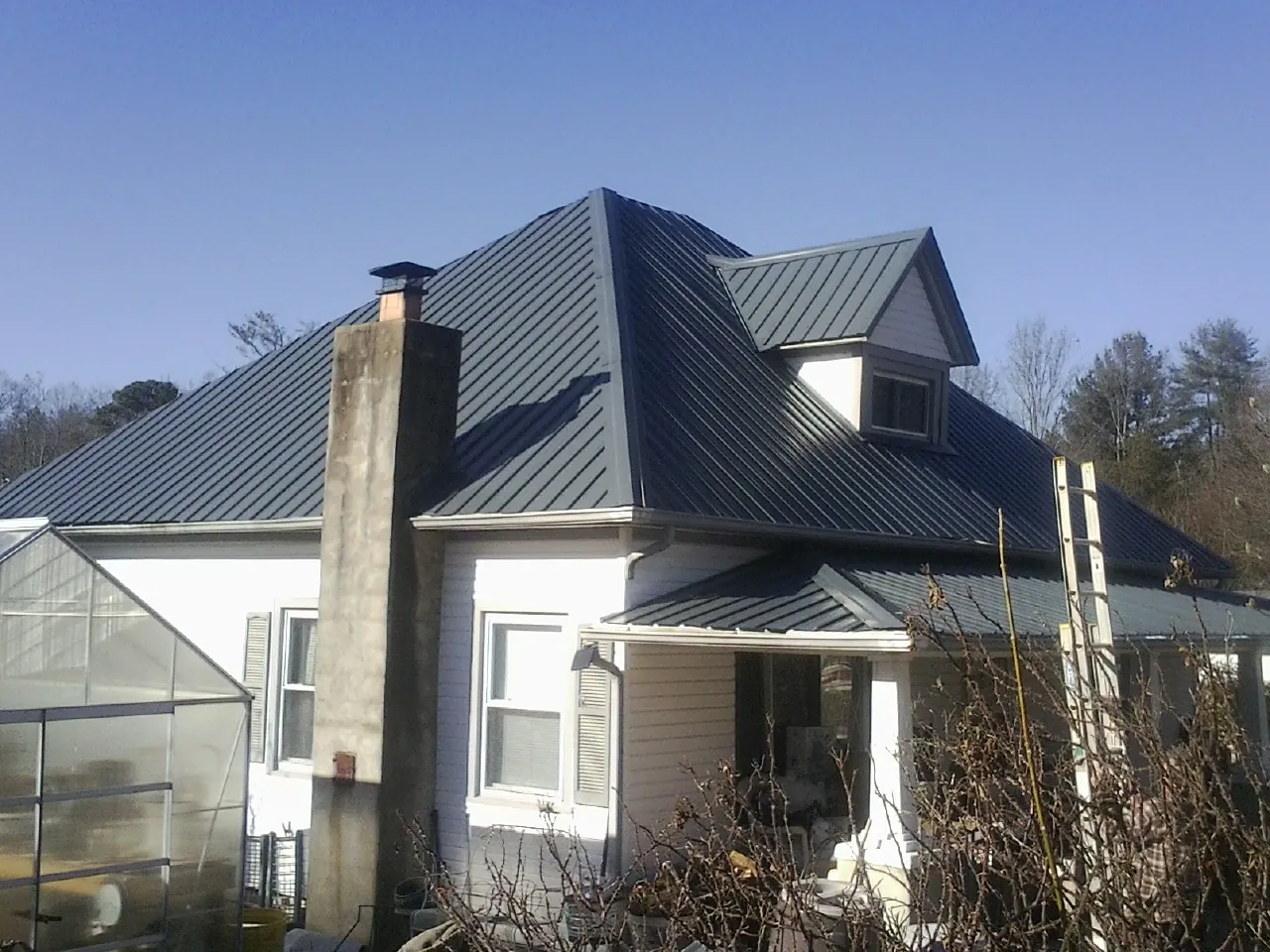 Dark blue standing seam metal roof on a white farmhouse with dormer — Slate & Tile Roof Repair by Roofing Brothers in Calumet
