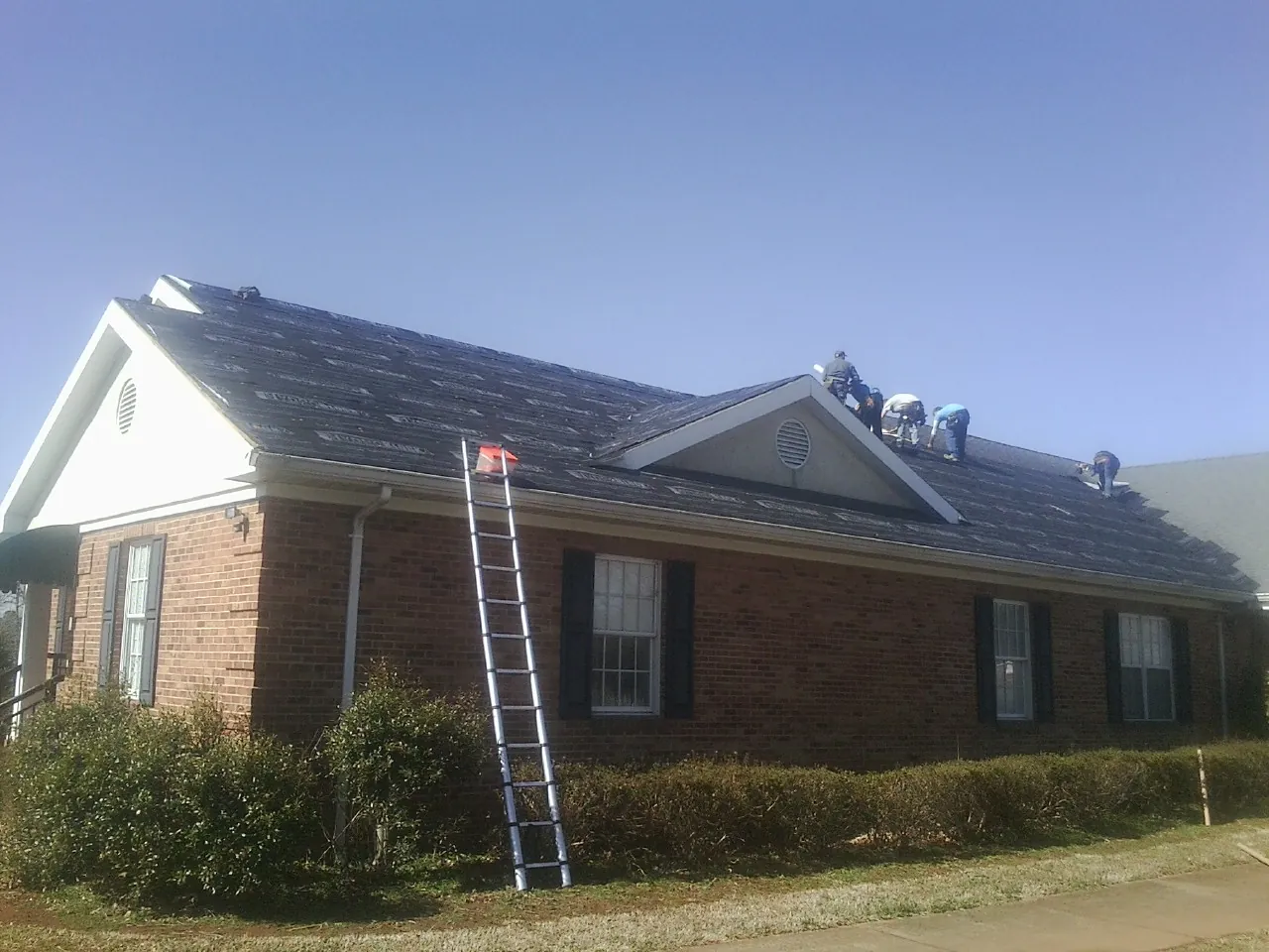 Crew tearing shingles off a brick ranch roof with a ladder set — Metal Roof Repair work by our crew in Calumet