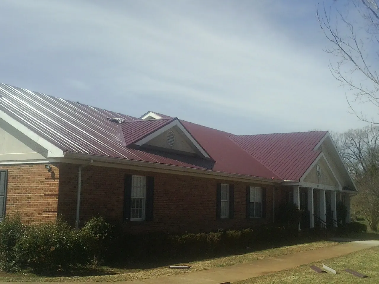 Red metal roof with gabled entries on a long brick building, from a Hail Damage Roof Repair job in Calumet