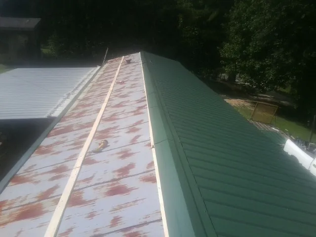 Old rusted panels beside newly installed green metal roofing — Wind Damage Roof Repair by Roofing Brothers in Calumet
