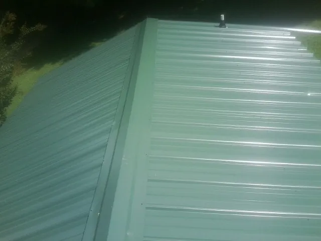 New green metal panels meeting at the ridge of a roof — Flat Roof Repair work by our crew in Calumet