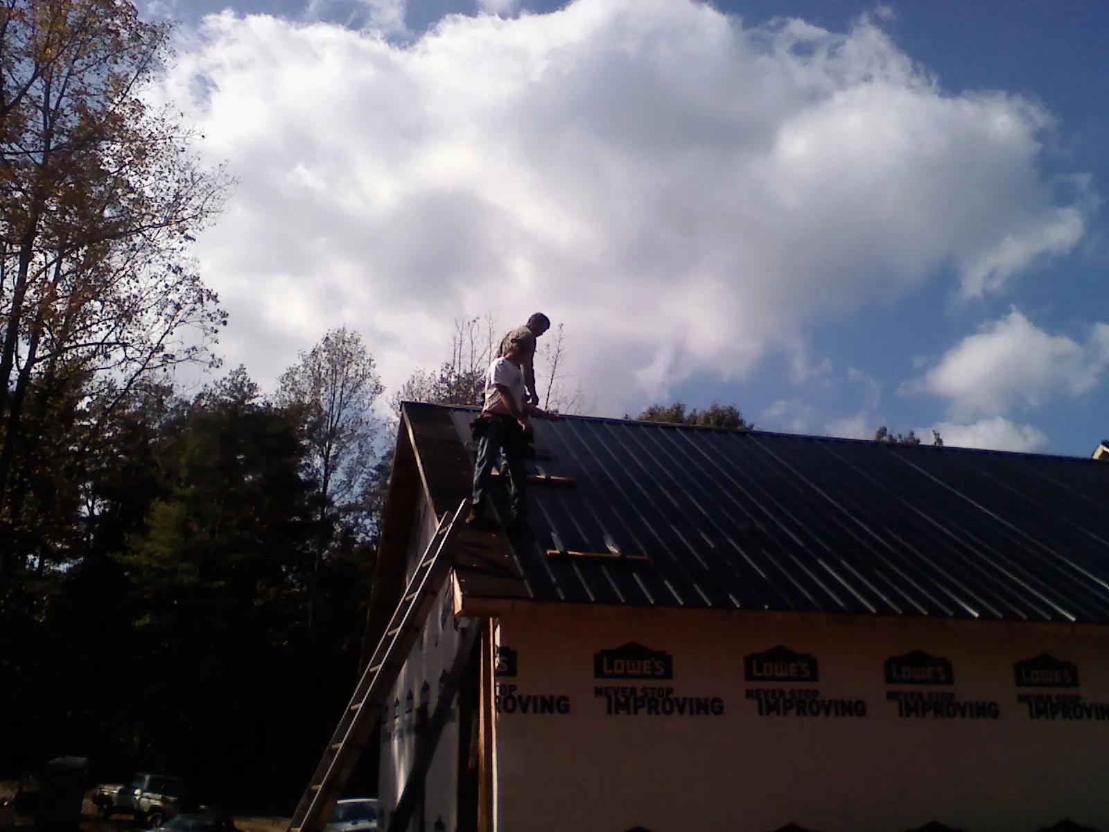 Roofer fastening dark metal panels high against a cloudy sky, from a Roof Inspection job in Calumet