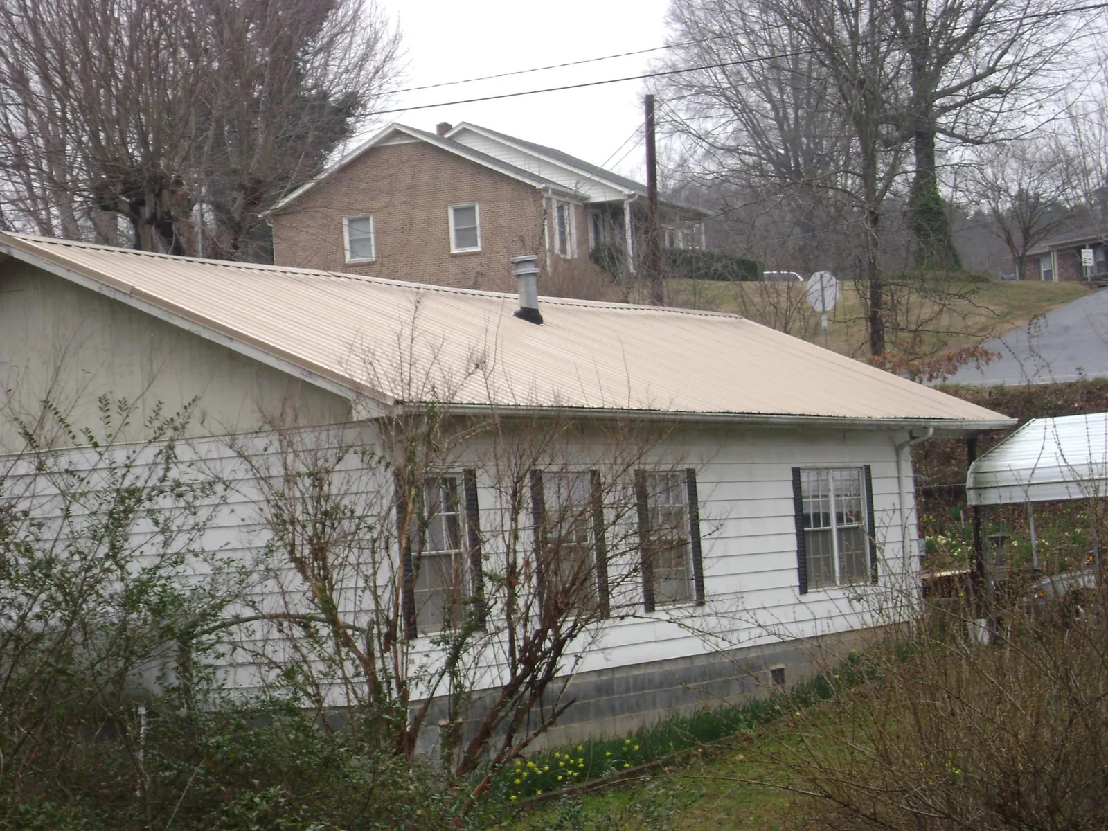 Tan metal roof on a white sided house set into a hillside — Commercial Roofing by Roofing Brothers in Calumet