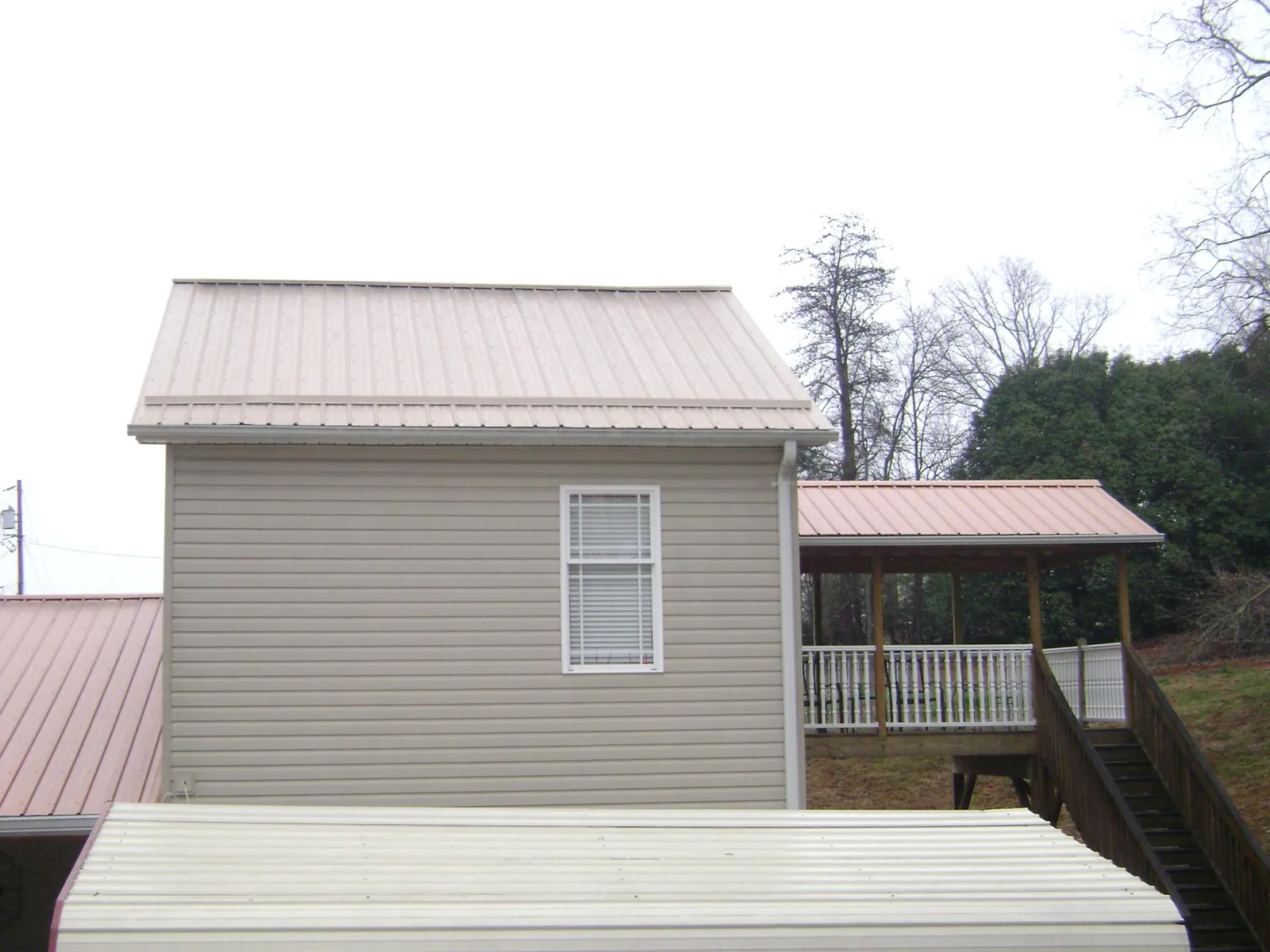Tan metal roofs on a two story addition and attached porch, from a Roof Replacement job in Calumet